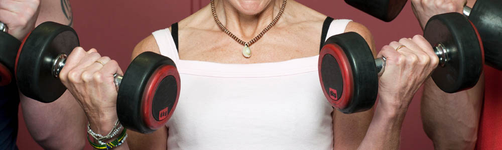 Close-up of torso of woman holding two dumbbells in front of her chest, with two men on either side of her